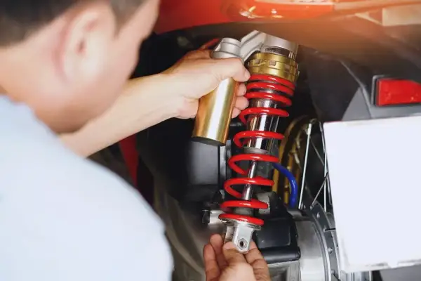 Mechanik dokonuje wymiany amortyzatorów tył w skuterze. Złoty element jest montowany do czerwonej sprężyny.