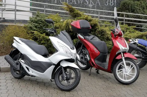 Dwa skutery, biały i czerwony, stoją na mokrym chodniku. Pytanie: co ile wymiana oleju w skuterze 50?